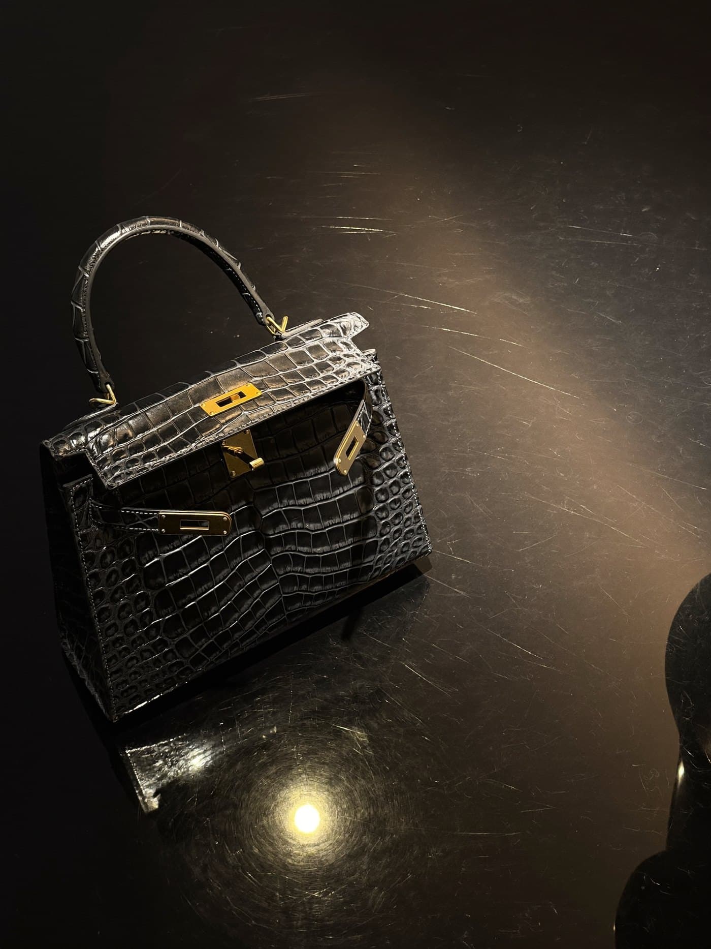 A black crocodile leather handbag with gold hardware under a single spotlight